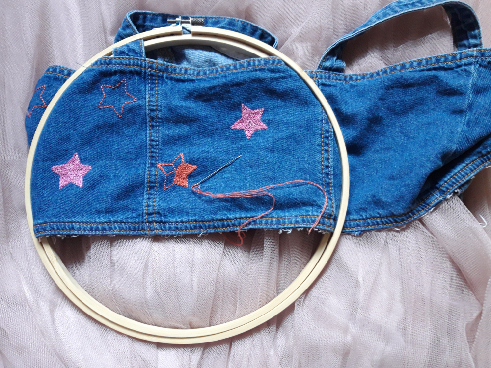 Embroidered pink and orange stars on blue denim fabric in embroidery hoop
